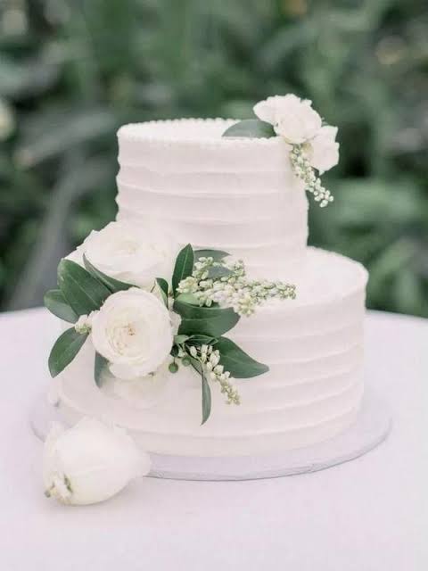 Tall ivory three-tier wedding cake decorated with fresh white blossom